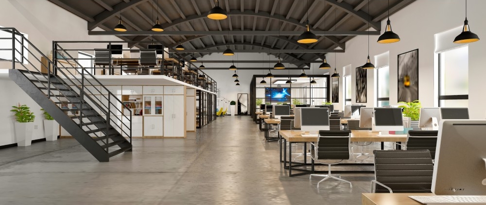 A modern, open office layout with concrete floors, high industrial ceilings, a loft, and rows of desks with computers.