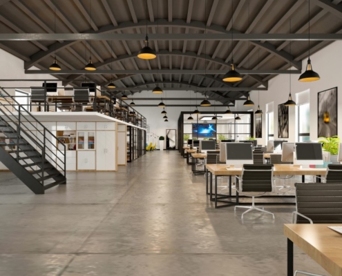 A modern, open office layout with concrete floors, high industrial ceilings, a loft, and rows of desks with computers.