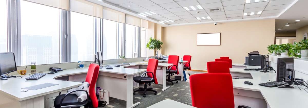 An office showcasing two parallel rows of office desks. There is a red chair and a computer at each station.