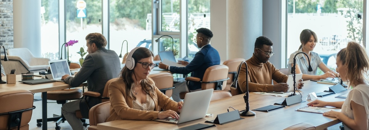 Several employees sitting at shared desk stations in an office with an open-plan layout. Everyone is hard at work.