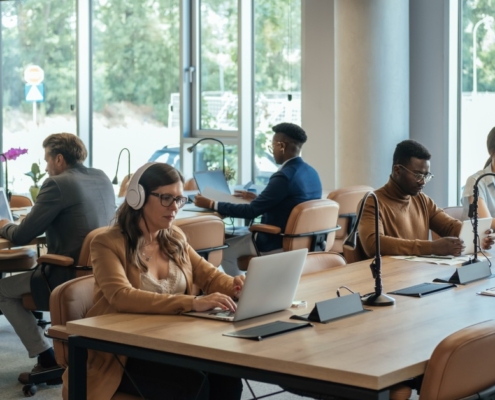 Several employees sitting at shared desk stations in an office with an open-plan layout. Everyone is hard at work.