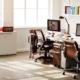 An office with two desks and brown chairs. An L-shaped workspace with cabinets is on the opposite side of the desks.