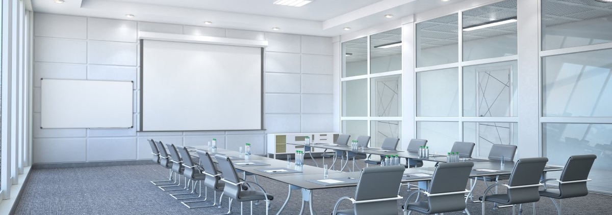 A large conference room with the table and chairs in a U-shaped layout. A projector and whiteboard are in the front of the room.