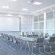 A large conference room with the table and chairs in a U-shaped layout. A projector and whiteboard are in the front of the room.