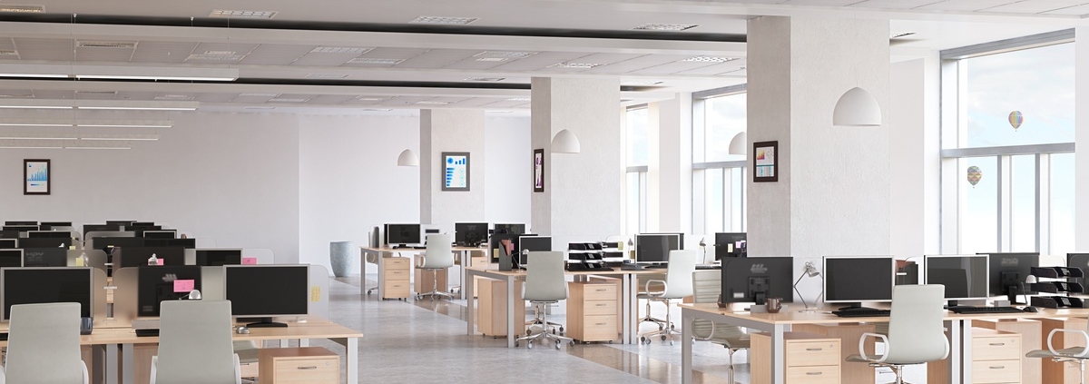 A large, sleek office interior with several workstations. Each station has a computer screen, file cabinet, and office chair.