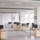 A large, sleek office interior with several workstations. Each station has a computer screen, file cabinet, and office chair.