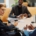 A businesswoman in a wheelchair sits at a table with two other men. She holds a coffee cup in one hand.