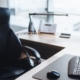 A brightly lit office space with a clean L-shaped desk. A black desk chair sits in front of the desk.