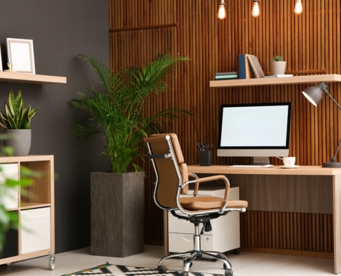 A modern office with plants and a computer desk. Various shelving, including floating shelves and a cabinet on wheels, is present.