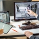 Two people sit next to each other at a computer desk. The man points to an office layout on the desktop while the woman holds a tablet.