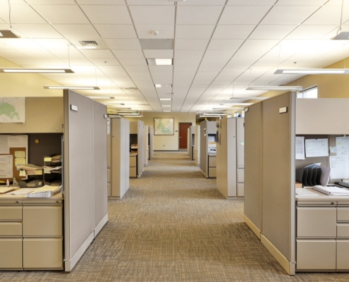 A modern office with several cubicles on either end of a makeshift hallway. The cubicles are filled with personal items.
