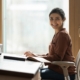 A woman sits at an ergonomically designed desk. The desk surface is slightly angled, and she sits in a chair made with lumbar support.