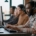 A group of co-workers sits in a line in front of computers. Each person is wearing a headset with a microphone.