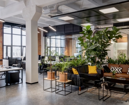 A modern office with tons of potted plants. There are several workstations, a conference room, and couches.