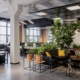A modern office with tons of potted plants. There are several workstations, a conference room, and couches.