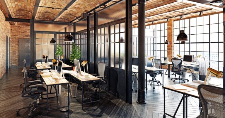 There is a large room with a partition in the middle separating the two halves of the room. Each side has desks and chairs.
